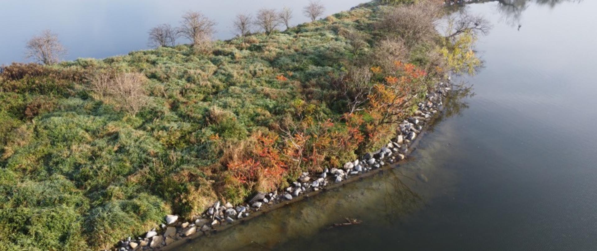 Zdjęcie prezentuje podłużną wyspę otoczoną wodą. Widoczne kamienne umocnienia brzegu.