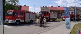 Na zdjęciu widać pojazdy pożarnicze stojące na parku w Kolnie, rodzina z dziećmi spaceruje.
