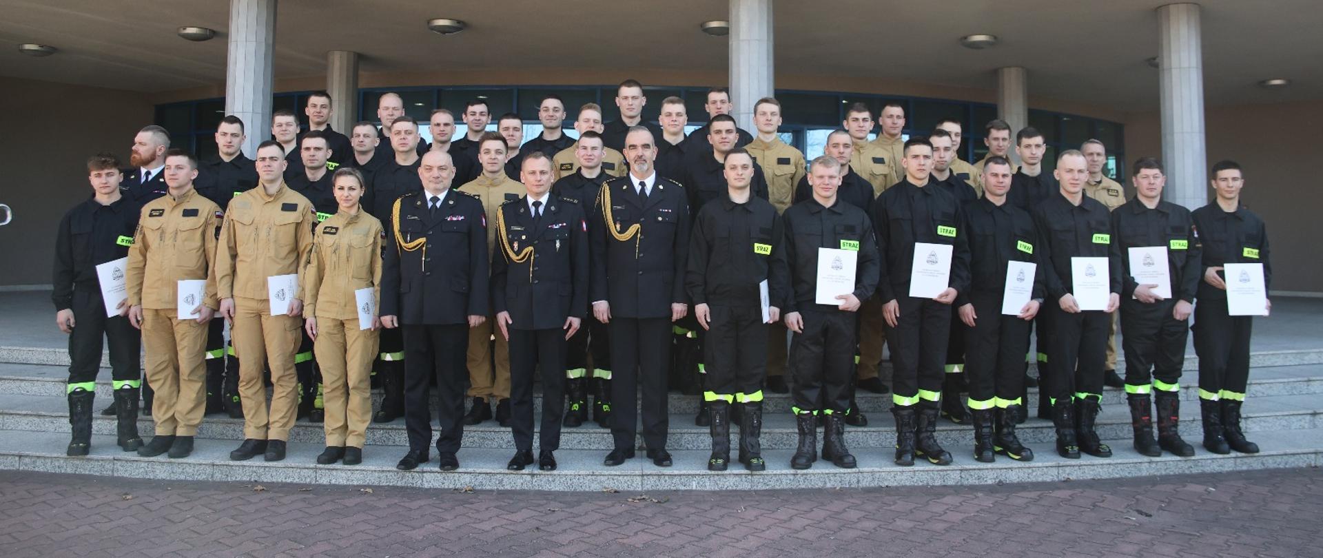 Pamiątkowe zdjęcie grupowe funkcjonariuszy PSP na zakończenie szkolenia podstawowego w zawodzie strażak w towarzystwie Komendanta Centralnej Szkoły PSP, dwóch Zastępców Komendanta Centralnej Szkoły PSP oraz trzech funkcjonariuszy CS PSP