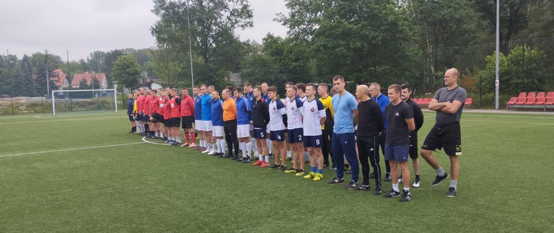 Strażacy w strojach sportowych stoją na boisku podczas zbiórki.