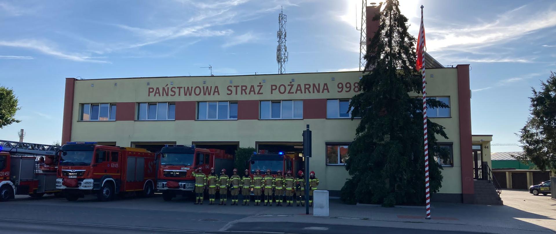 Na zdjęciu widać strażaków oddających hołd na tle wozów strażackich 