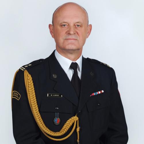 Na zdjęciu brygadier Maciej Łubisz, Zastępca Komendanta Powiatowego Państwowej Straży Pożarnej w Pabianicach. Występuje w umundurowaniu wyjściowym ze sznurem. Na lewej piersi przypięte baretki. Na prawej piersi od góry znajduje się imiennik oraz absolwentka Szkoły Głównej Służby Pożarniczej.