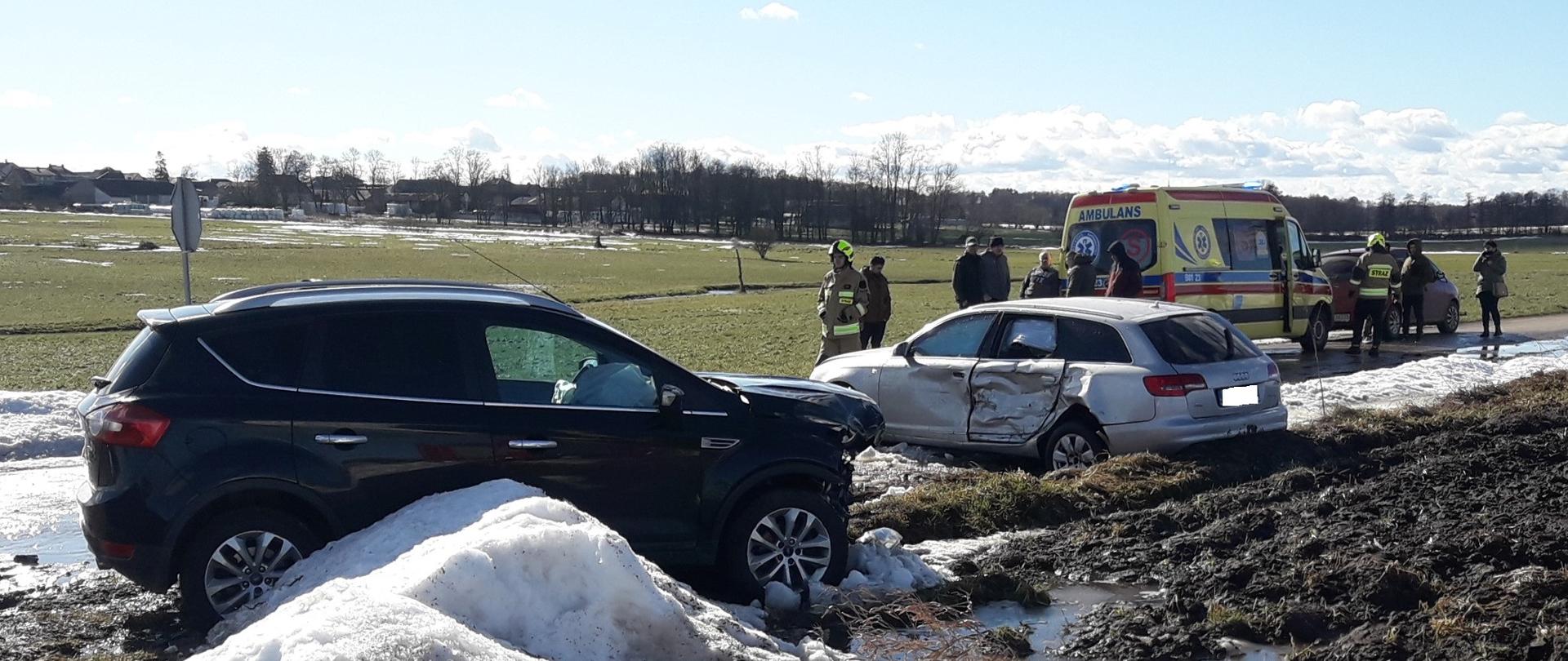 Uszkodzone dwa samochody osobowe. W tle karetka pogotowia i strażacy OSP.