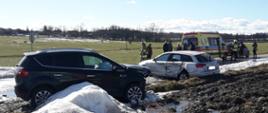 Uszkodzone dwa samochody osobowe. W tle karetka pogotowia i strażacy OSP.