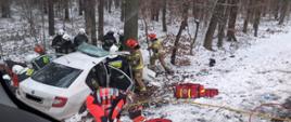 Na zdjęciu widoczny samochód osobowy, który uderzył w drzewo. Strażacy udzielają pomocy osobom poszkodowanym.