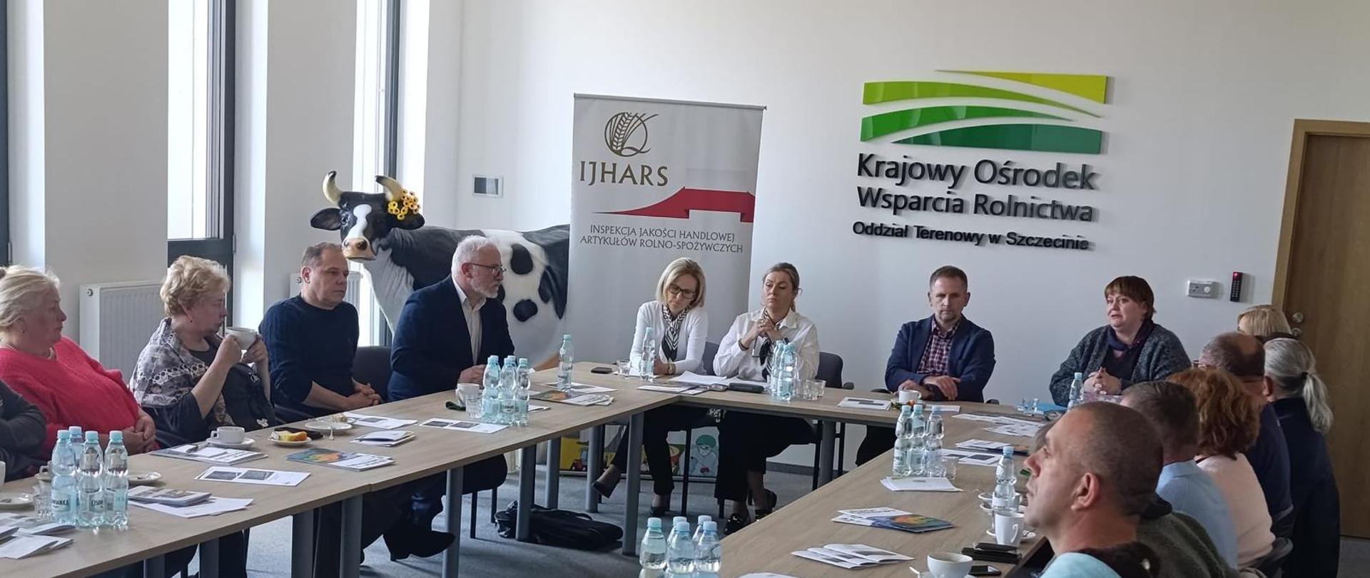 Uczestnicy siedzą przy stole konferencyjnym i prowadzą dyskusję; w tle widoczny baner IJHARS oraz KOWR.