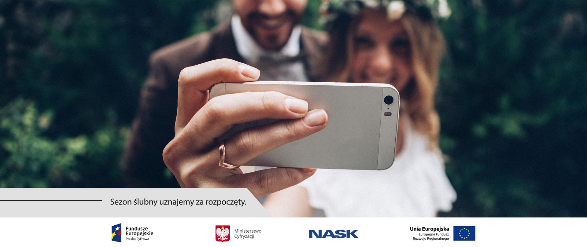 Grafika. Pani Młoda i Pan Młody robią sobie wspólne zdjęcie, tzw. selfie. Obok napis: Sezon ślubny uznajemy za rozpoczęty.