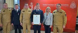 Zdjęcie przedstawia osoby funkcyjne na tle loga PSP w związku z uroczystym włączeniem OSP Okup do Krajowego Systemu Ratowniczo Gaśniczego. Od lewej stoją. Komendant Wojewódzki PSP w Łodzi, Prezes OSP Okup, Zastępca Komendanta Głównego PSP, dh. z OSP Okup, Zastępca Burmistrza Łasku, Komendant Powiatowy PSP w Łasku.
