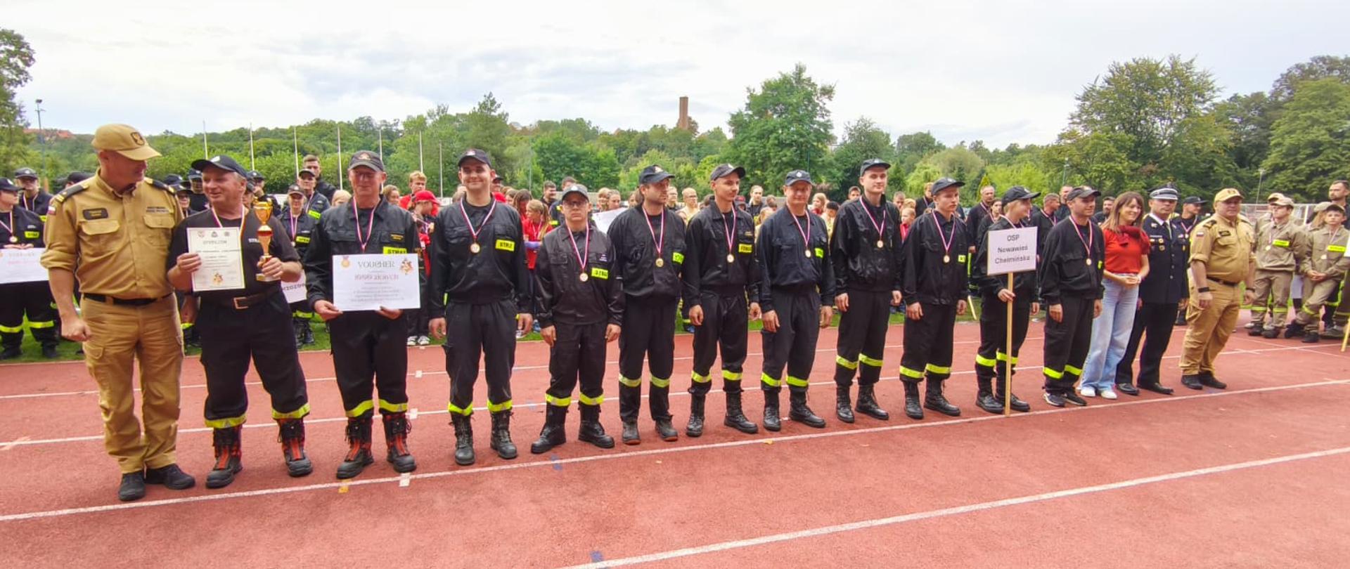Powiatowe Zawody Sportowo-Pożarnicze OSP - Chełmno 2025 - zdjęcie wykonano na Stadionie Miejskim w Chełmnie, druhowie podczas dekoracji zwycięzców;