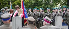Na cmentarzu między rzędami betonowych krzyży stoją ludzie w polskich wojskowych mundurach.