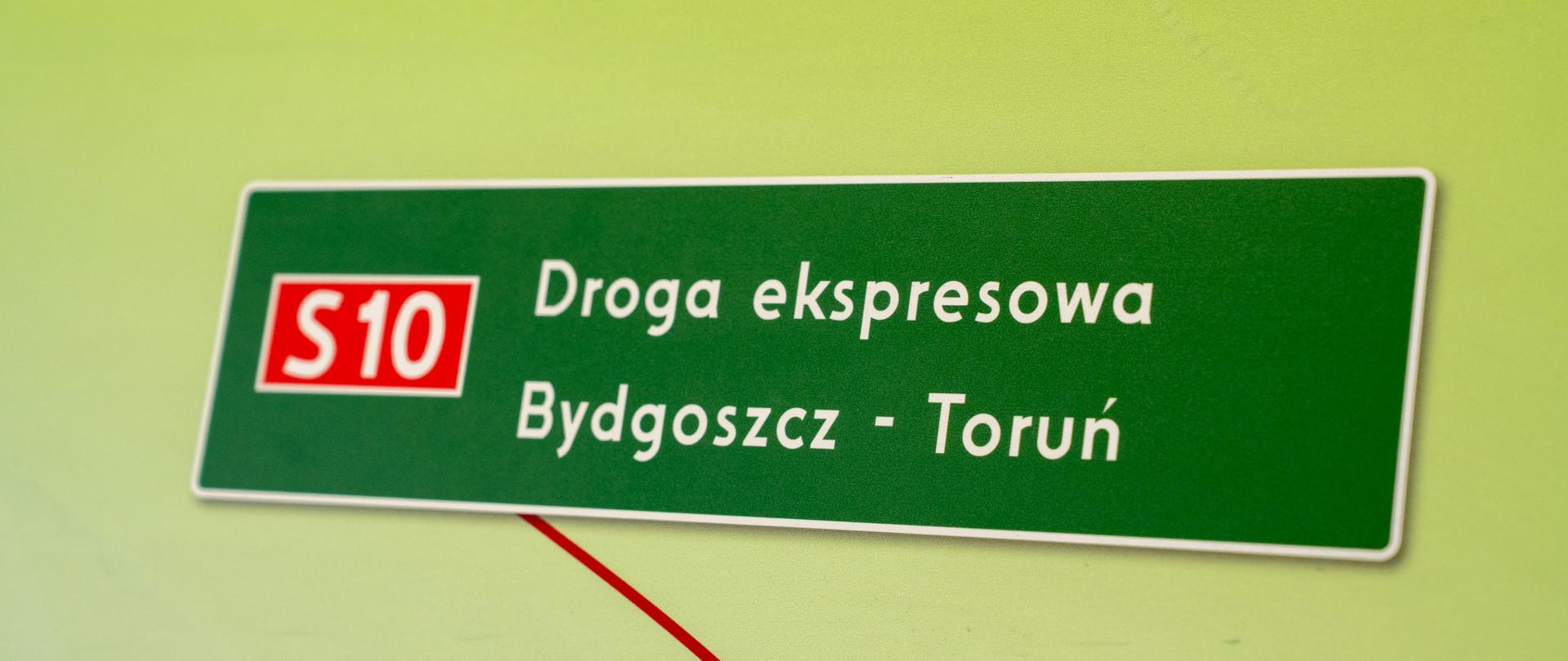 Tablica kierunkowa wskazuje trasę łączącą te dwa kluczowe miasta województwa kujawsko-pomorskiego. Tego typu oznakowanie jest charakterystyczne dla węzłów komunikacyjnych oraz odcinków budowanej drogi ekspresowej S10, która ma usprawnić ruch na tym odcinku.