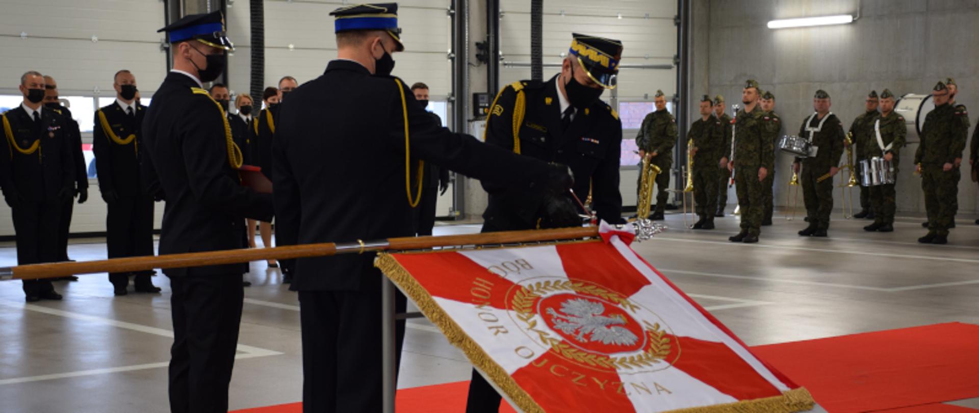 Zastępca KG PSP wbija gwoździe w drzewiec sztandaru