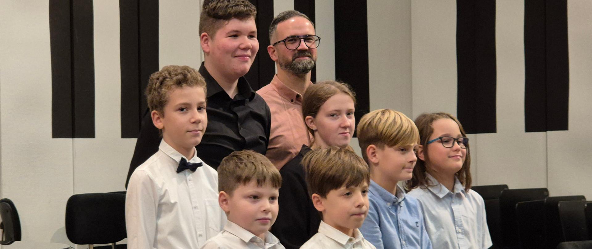 Nauczyciel z uczniami stoi na scenie.