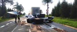 Zdjęcie przedstawia samochód ciężarowy z naczepą, tuż za nim rozbite pojazdy oraz funkcjonariuszy Policji.
