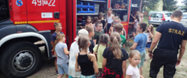 Na pierwszym planie widoczna grupka dzieci oglądająca wóz bojowy Państwowej Straży Pożarnej widoczny w tle