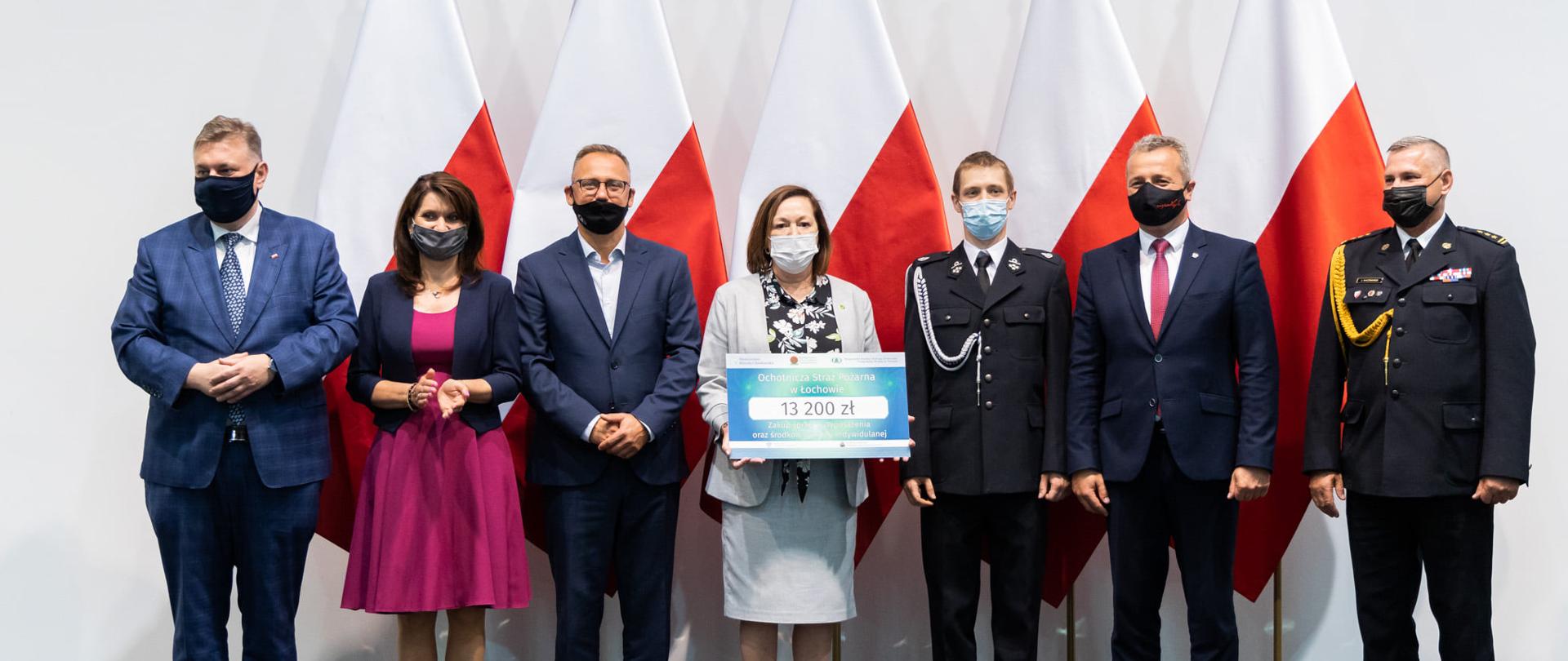 W tle zdjęcia flagi państwowe, Zdjęcie przestawia wręczenie vouchera w ramach programów: dofinansowanie zakupu sprzętu dla jednostek OSP oraz EKOSTRAŻAK dla jednostki OSP Łochowo. Na zdjęciu przedstawiciel OSP Łochowo, Wojewoda Mikołaj Bogdanowicz, Kujawsko-Pomorski Komendant Wojewódzki PSP st. bryg. Jacek Kaczmarek, Prezesem Wojewódzkiego Funduszu Ochrony Środowiska i Gospodarki Wodnej Ireneusz Stachowiak oraz Posłowie Ewa Kozanecka oraz Piotr Król.