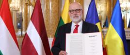 Przewodniczący Maciej Świrski stoi na tle flag, przedstawia podpisaną deklarację