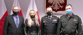 Zdjęcie pamiątkowe. Od lewej Stanisław Ręcławowicz - Dyrektor Biura ds. Ochrony Ludności i Obrony Cywilnej KG PSP, dr Monika Wyszomirska – pełnomocnik Międzyuczelnianego Instytutu Konserwacji i Restauracji Dzieł Sztuki, Zastępca Komendanta Głównego Państwowej Straży Pożarnej nadbryg. dr inż. Adam Konieczny oraz st.bryg.dr Dariusz Wróblewski – doradca Komendanta Głównego PSP. W tle flagi narodowe oraz godło państwowe