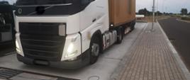 Od lewej: rozłożone inspekcyjne wagi w zatoce kontrolnej i stojący przed nimi ciągnik siodłowy z podpiętą naczepą - kontenerem. Obok stoi oznakowany furgon mazowieckiej Inspekcji Transportu Drogowego z otwartymi drzwiami bocznymi do przestrzeni biurowo - kontrolnej.