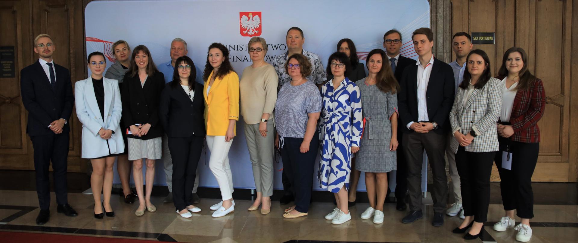 Kilkanaście osób stojących na tle ścianki z napisem ministerstwo finansów.