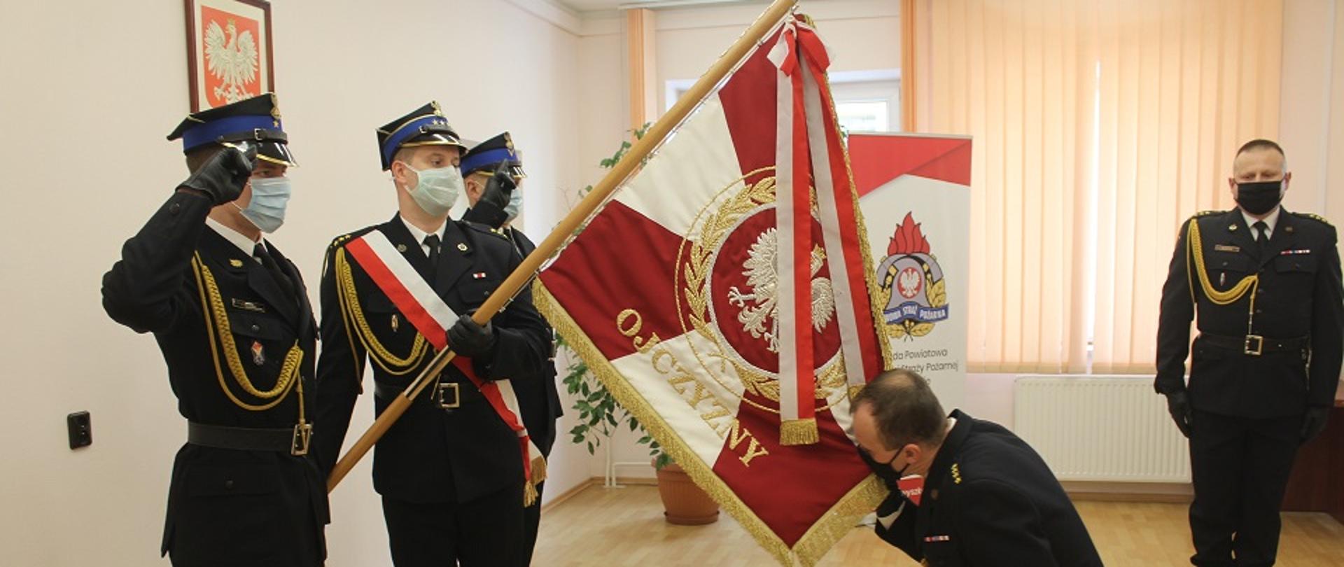 Komendant klęczący przed pocztem sztandarowym i całujący go.