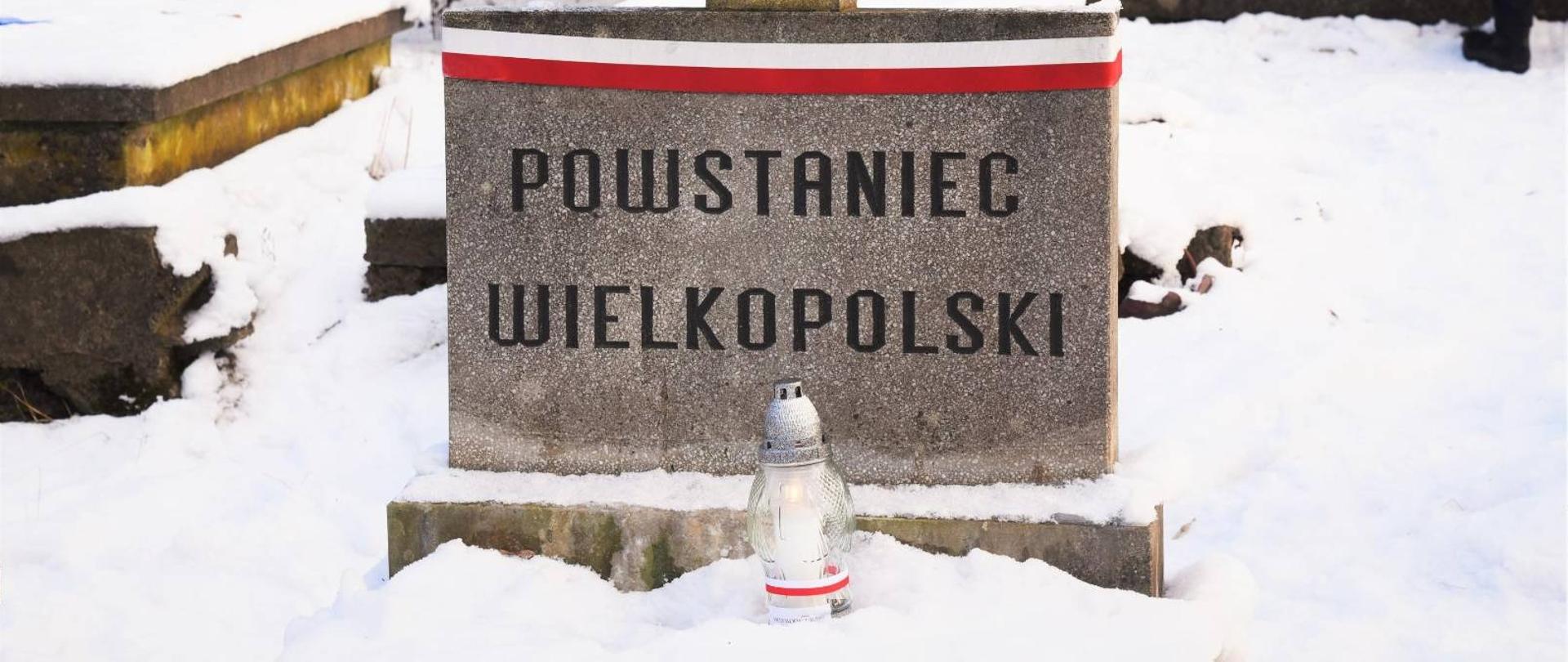 Grób z napisem "Powstaniec Wielkopolski" z biało-czerwoną wstążką i zapalonym zniczem 