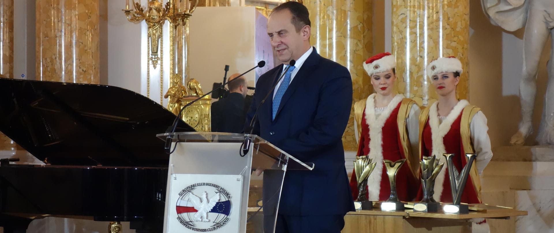 minister stoi przy mównicy, w tle statuetki nagród