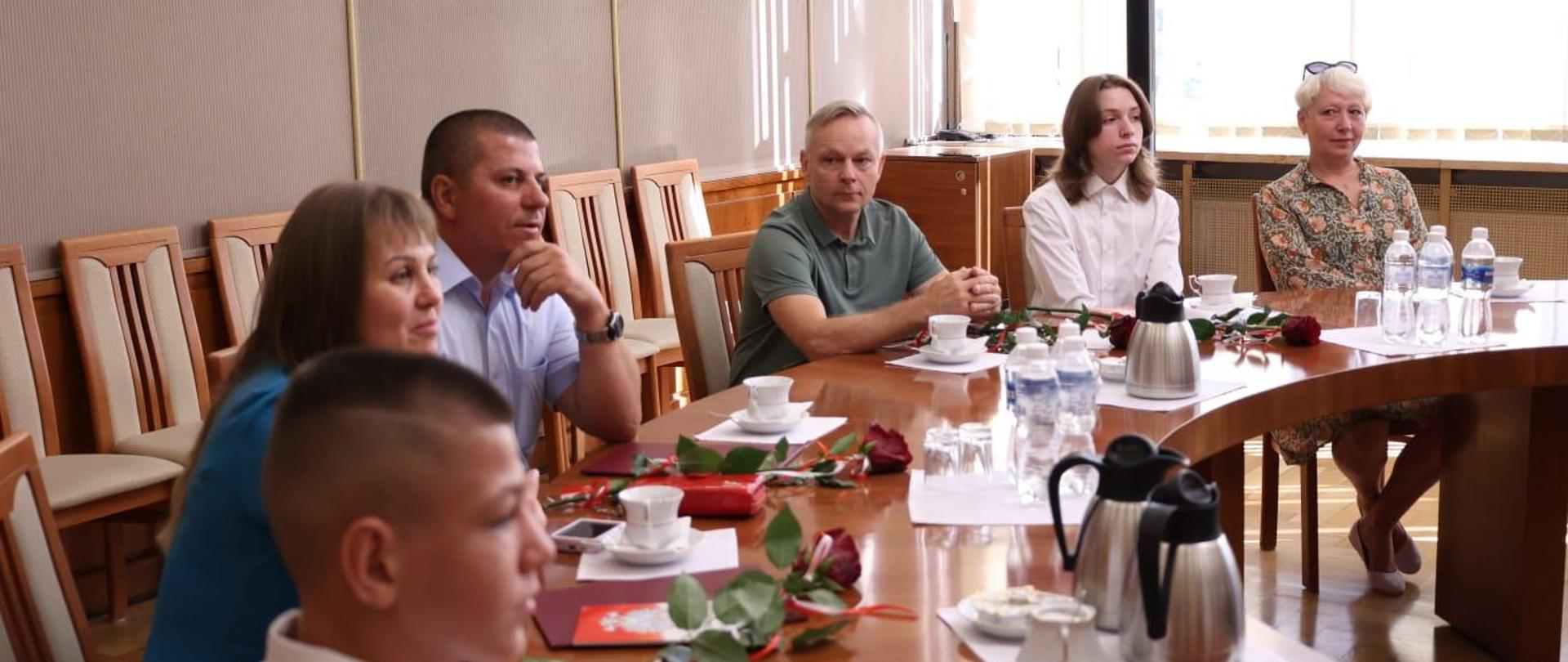 Nowi obywatele, uczestnicy uroczystości siedzą przy okrągłym stole w Sali Złotej. Na stołach leżą ich akty nabycia obywatelstwa oraz otrzymane róże. 