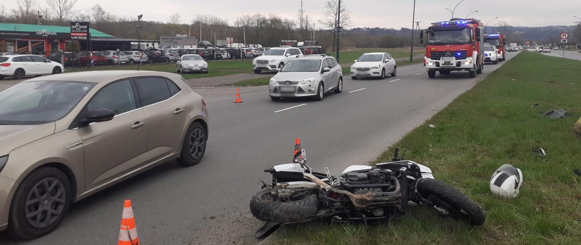 Widok leżącego motocykla a obok samochody.