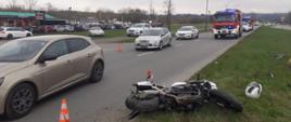 Motocykl leży na pasie zieleni oraz częściowo na drodze.