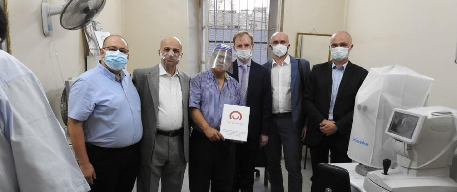 Mężczyźni pozują na tle przekazanego sprzętu medycznego z logo programu Polska pomoc