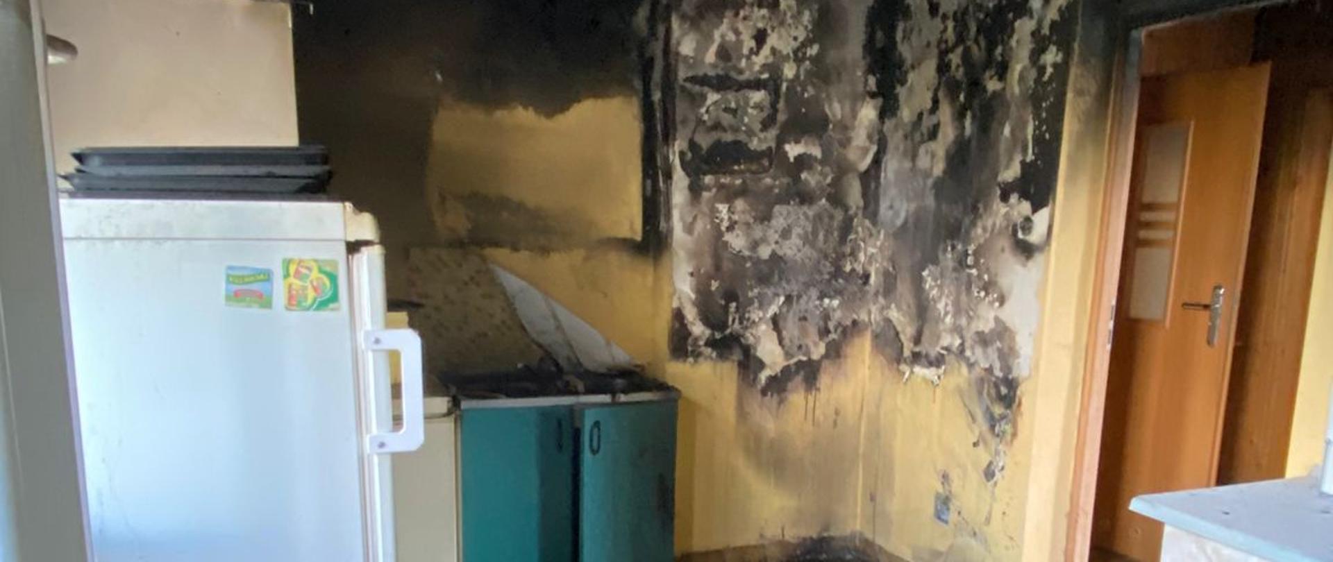 Wnętrze kuchni po ugaszeniu pożaru. Po lewej stronie stoi lodówka, po środku i po prawej stronie szafki. Widoczne nadpalenie sufitu.