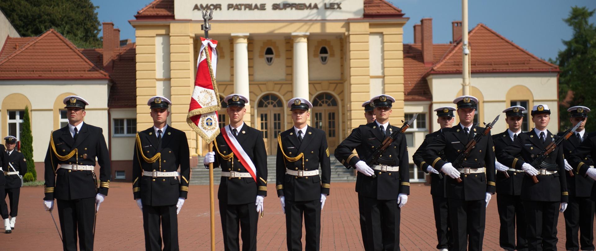Poczet sztandarowy - studenci w galowych mundurach stoją przed budynkiem akademii.