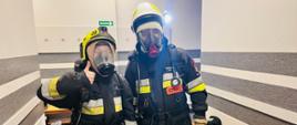 Zdjęcie przedstawia 2 kandydatów na strażaków OSP podczas próby wysiłkowej. W pełnym umundurowaniu i aparatach ochrony dróg oddechowych.