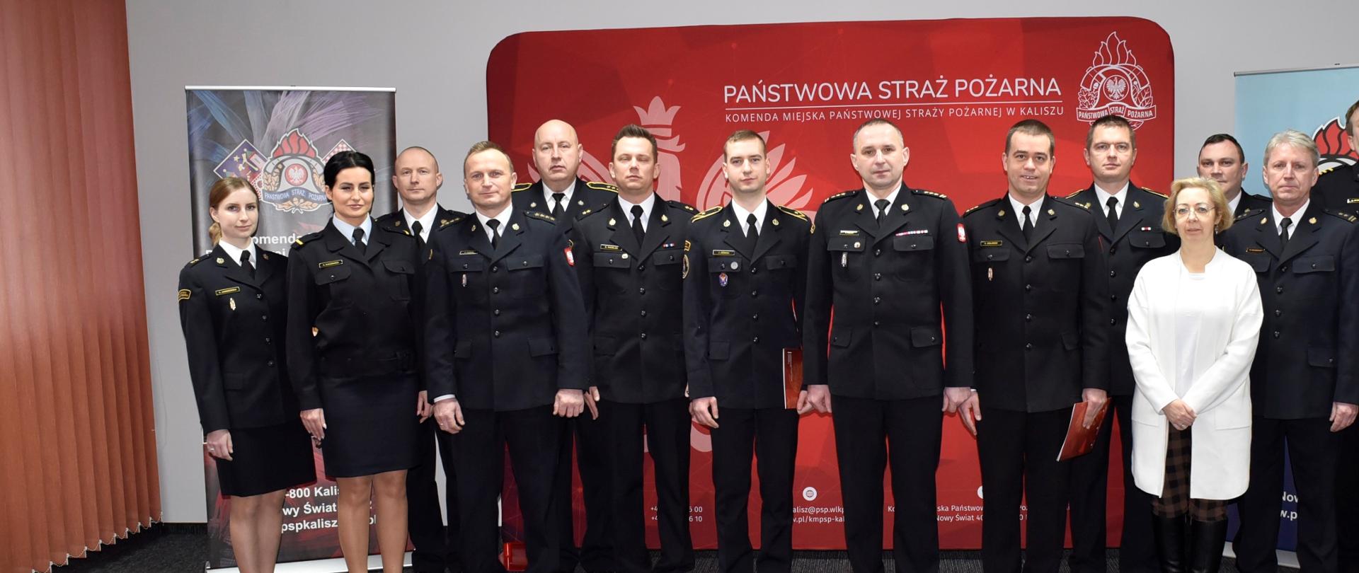 Na zdjęciu widać funkcjonariuszy PSP w umundurowaniu wyjściowym. Zdjęcie w pomieszczeniach komendy. Oświetlenie sztuczne. Na podłodze dywan.