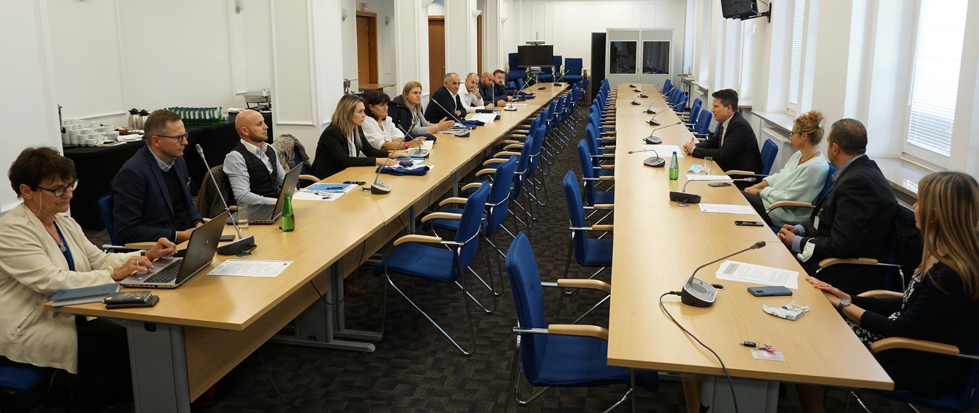 przy stołach które stoją wzdłuż sali siedzą uczestnicy spotkania, na stołach mikrofony i przy niektórych uczestnikach komputery przenośne (laptopy)