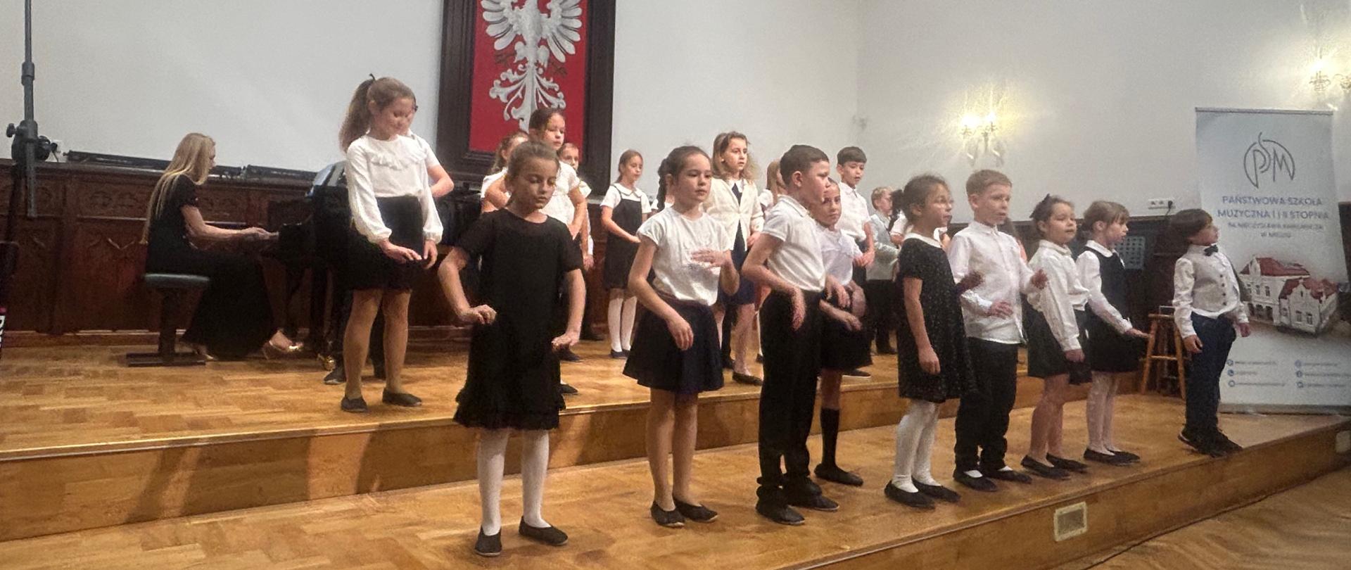 uczniowie klas pierwszych podczas pasowania na ucznia na scenie w sali królewskiej Psm Mielec