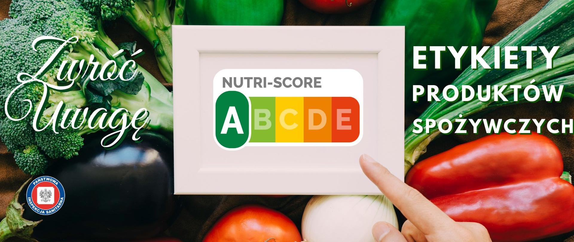 Palec wskazujący tabliczkę z oznaczeniem Nutri-score nad poukładanymi na stole różnokolorowymi warzywami