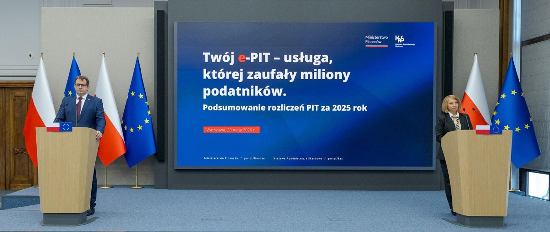 Dwie osoby stoją przy oddzielnych mównicach, a między nimi ekran z napisem „Twój e‑PIT – usługa, której zaufały miliony podatników” oraz informacją o podsumowaniu PIT za 2025 rok.