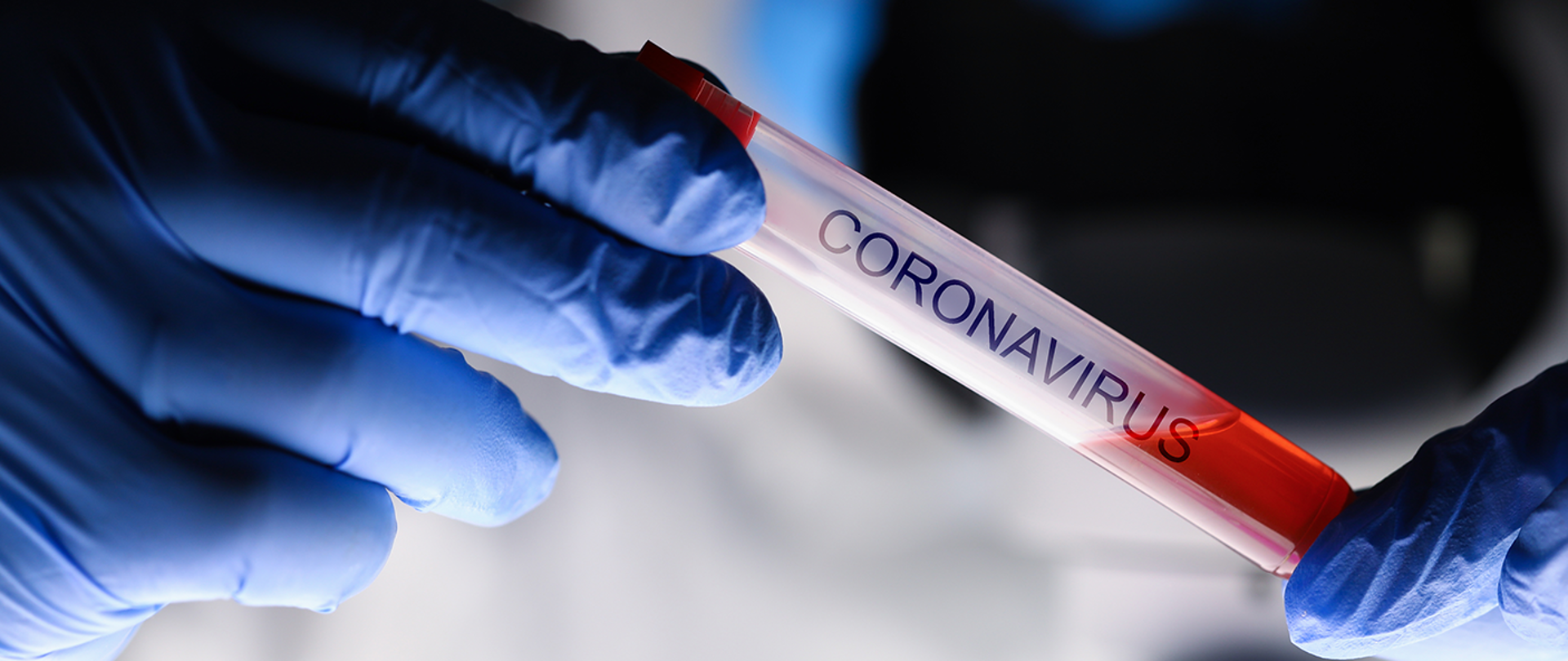 Ampułka z czerwoną substancją, podpisana "coronavirus", trzymana w rękach w niebieskich lateksowych rękawiczkach. 