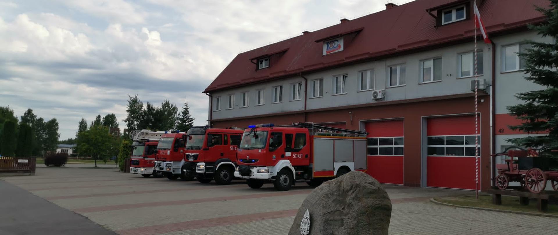 Pojazdy pożarnicze na sygnałach swietlno dźwiękowych przed budynkiem komendy