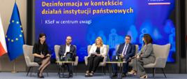 Panel dyskusyjny z udziałem pięciu osób siedzących na scenie w fotelach. Uczestnicy trzymają mikrofony i prowadzą rozmowę. W tle duży ekran z napisem: Dezinformacja w kontekście działań instytucji państwowych oraz podtytułem KSeF w centrum uwagi. W prawym górnym rogu widoczne logotypy HAI Human Answer Institute i Ministerstwa Finansów. Na scenie stoją małe stoliki z wodą i notatkami.