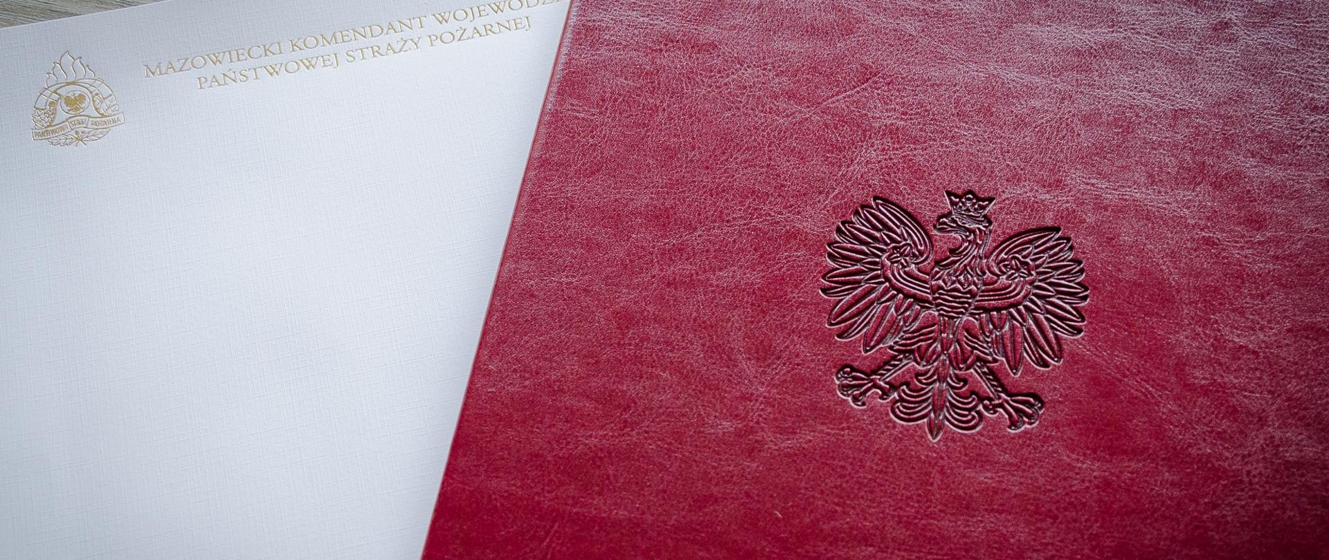 Po prawej stronie zdjęcia bordowa teczka z wytłoczonym godłem RP. Z lewej strony zdjęcia biała strona ze złotym logotypem PSP oraz napisem mazowiecki komendant wojewódzki PSP.
