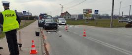 Na zdjęciu: na pierwszym planie funkcjonariusz Policji prowadzący swoje czynności, następnie jeden z pojazdów biorący udział w zdarzeniu, w oddali dwa samochody gaśnicze straży pożarnej, ruch na drodze wahadłowy, na drodze pozostałości po kolizji- plastiki, rozlane płyny eksploatacyjne.