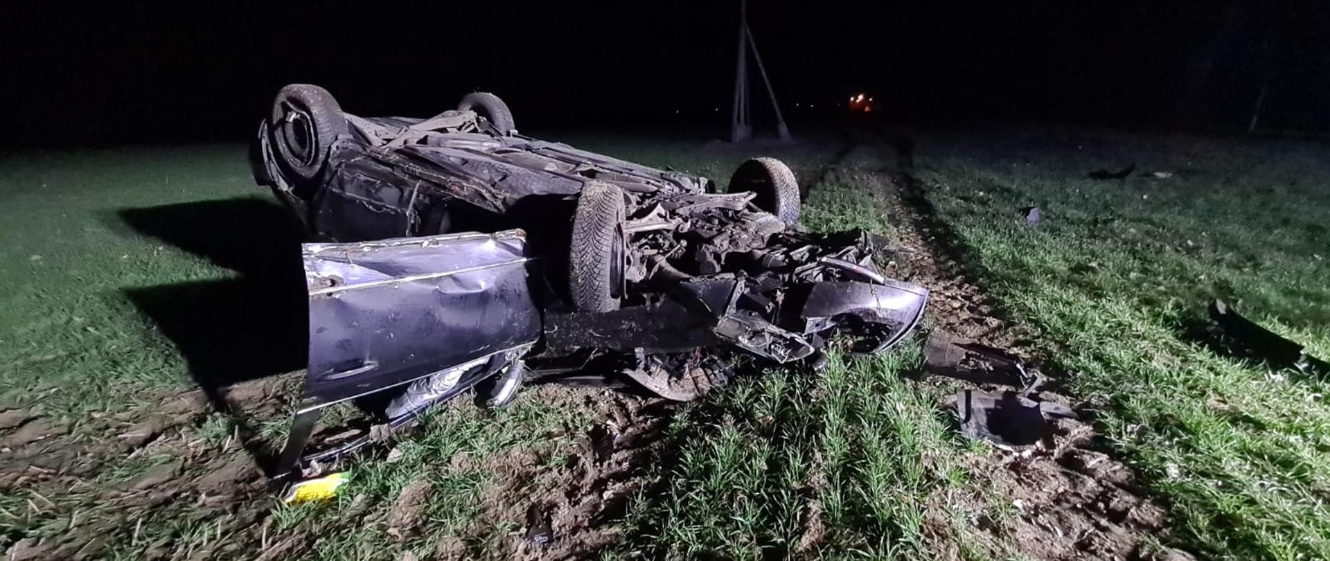 Widać uszkodzony ciemny samochód po dachowaniu na polu