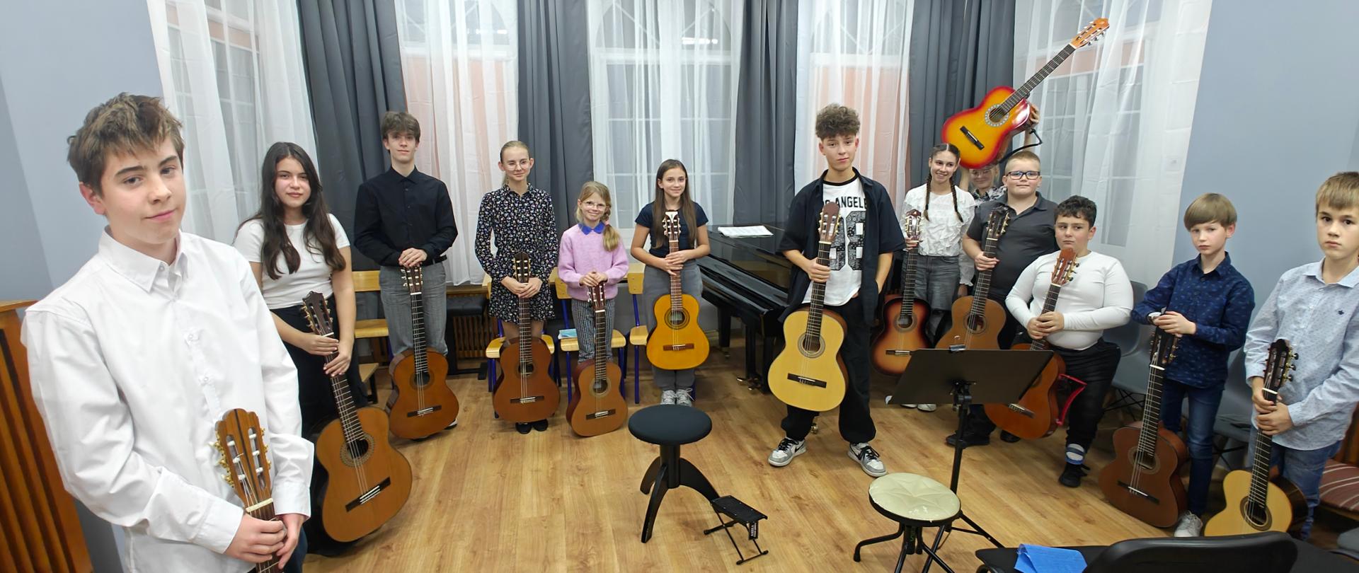 Zdjęcie przedstawiające wykonawców popisu klas gitary mgr Bartłomieja Filipowicza i mgr Sebastiana Środy, który odbył się 21 października 2025 r. w sali numer 3 tzw. "starego" budynku szkoły.