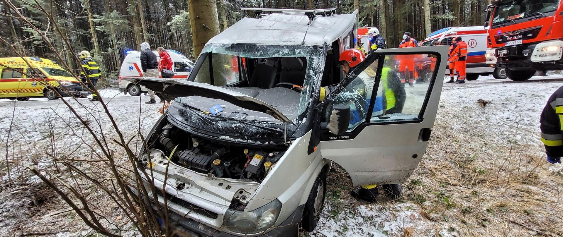 Bus poza drogą a w tle samochody służb ratowniczych.