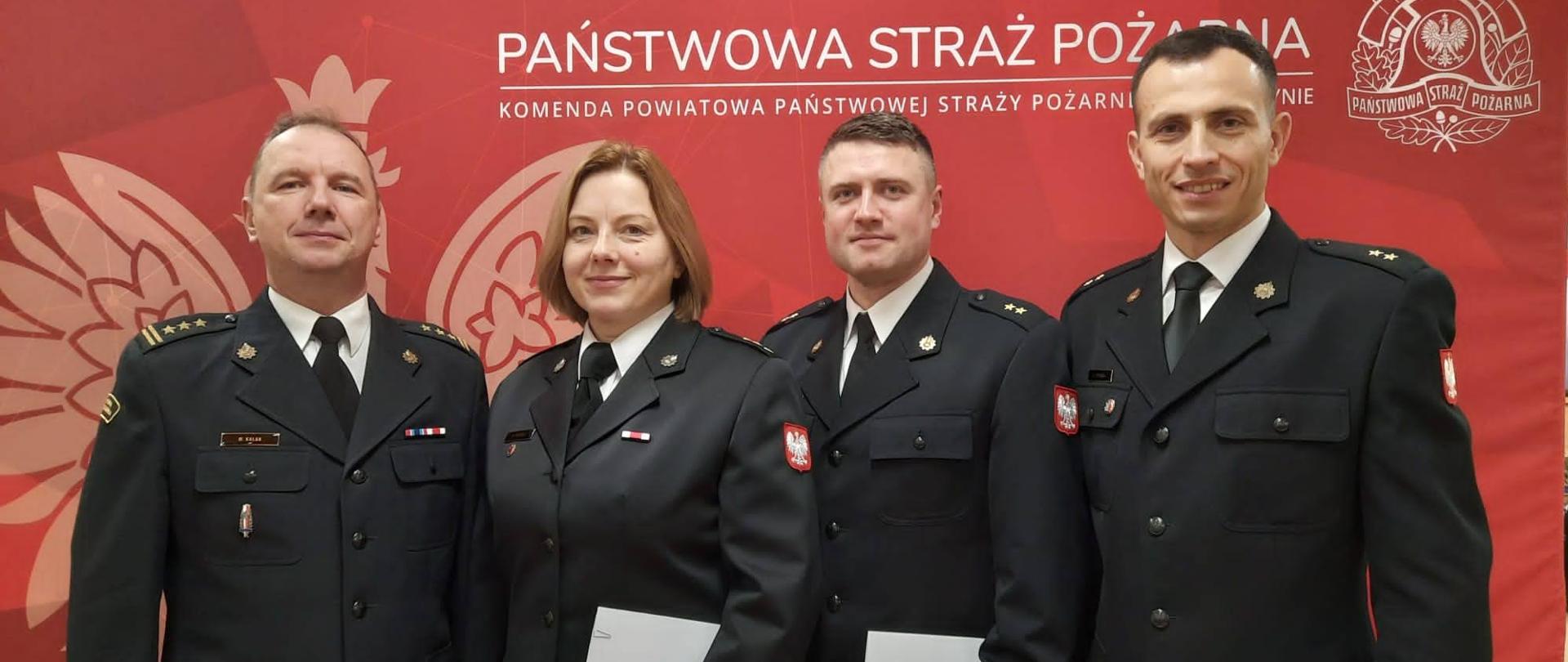 Na świetlicy komendy powiatowej zdjęcie grupowe awansowanych funkcjonariuszy z komendantem powiatowym PSP w Krotoszynie. Zdjęcie wykonane w umundurowaniu galowym na tle baneru Państwowej Straży Pożarnej