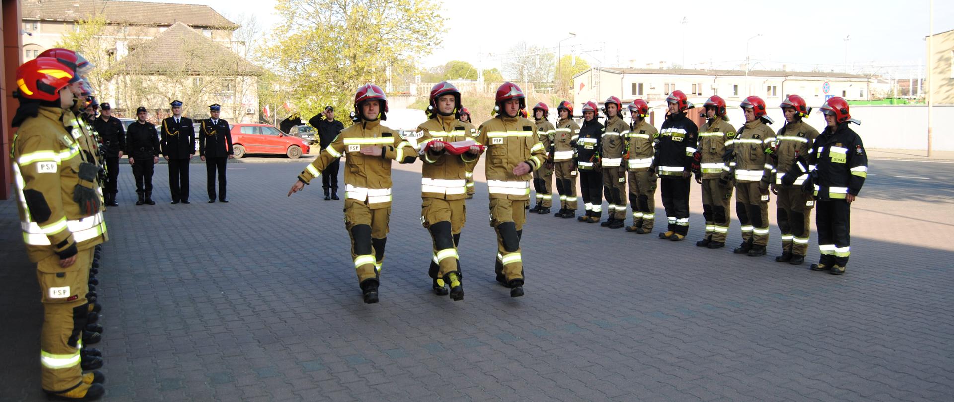 Pomiędzy dwoma szeregami strażaków, maszeruje poczet flagowy