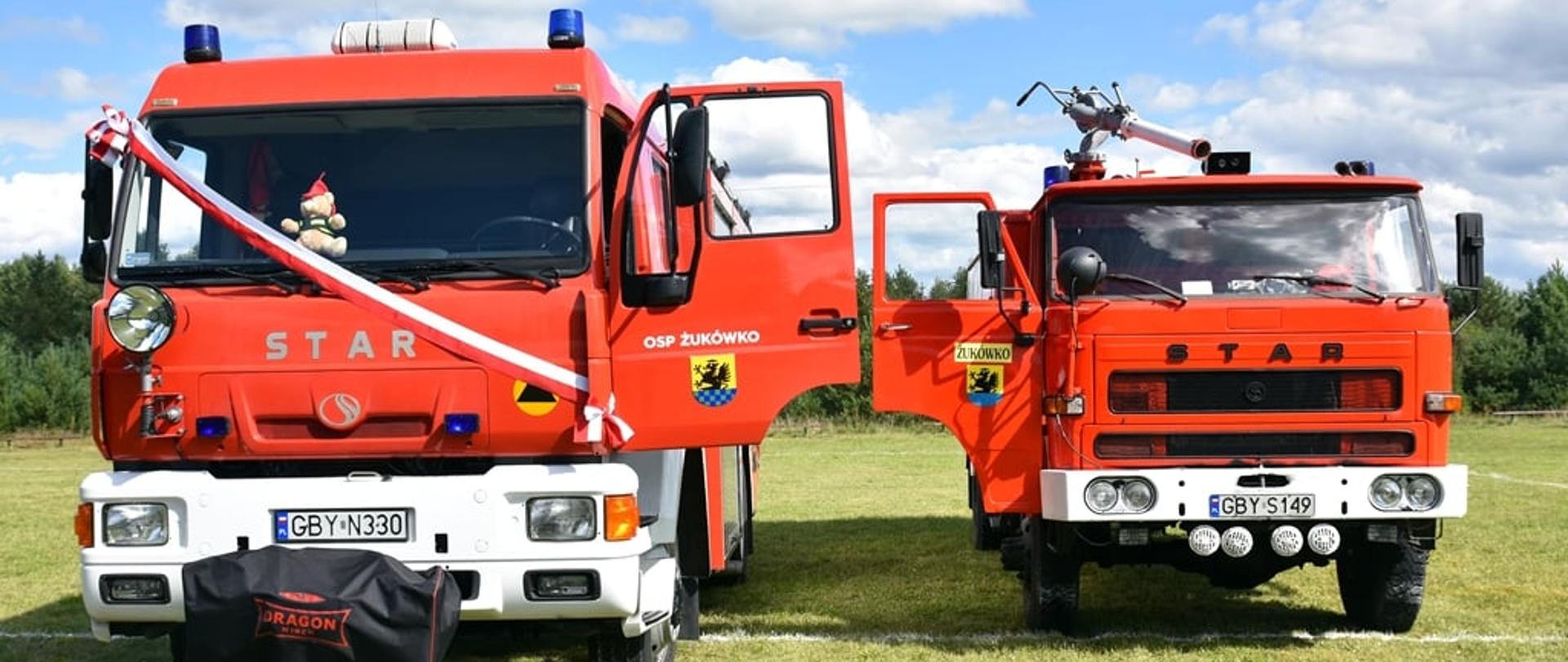 Zdjęcie przedstawia 2 samochody ratowniczo-gaśnicze marki STAR koloru czerwonego, samochód po lewej stronie jest z przewieszoną biało-czerwoną wstęgą oraz otwartymi drzwiami od strony kierowcy, natomiast samochód ustawiony z prawej strony ma otwarte drzwi od strony pasażera. Na otwartych drzwiach widnieją napisy OSP Żukówko oraz herb Gminy Parchowo